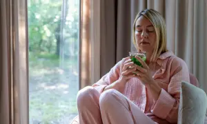 Frau in rosa Schlafanzug genießt einen frischen Pfefferminztee. Die Augen sind geschlossen, sie scheint die Ruhe zu genießen.