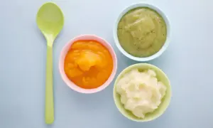Drei Schälchen mit Babynahrung: orangefarben, grün und weiß. Welcher Joghurt Baby ist wohl am leckersten? Ein grüner Löffel liegt daneben.