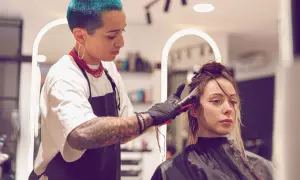 Friseurin mit blauen Haaren blondiert die Haare einer Kundin. Die Kundin wartet geduldig auf das Ergebnis, während die Friseurin sorgfältig arbeitet.