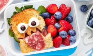 Ein lustiges Vesper-Essen Kita: ein Toast-Gesicht mit Wurst, Gurke und Beeren.