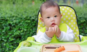 Ein süßes Baby isst im Hochstuhl. Der **Kalorienbedarf Baby 10 Monate** ist wichtig für seine Entwicklung.