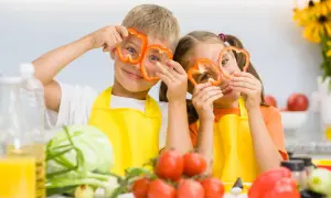 Zwei Kinder mit Paprikaringen vor den Augen, die Spaß beim Kochen haben. Gesunde Ernährung ist wichtig für den **Kalorienbedarf Kleinkind**.
