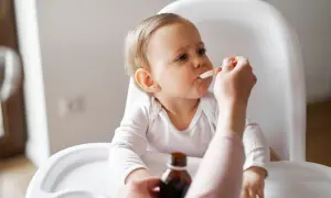 Ein Baby im Hochstuhl erhält Medikamente per Löffel. Die Eltern wechseln zwischen Ibuprofen und Paracetamol alle 4 Stunden, um Fieber zu senken.