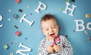 Lachendes Baby mit Brille inmitten von Buchstaben. Bald beginnt die spannende Reise, ab wann sprechen Kinder?