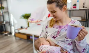 Mutter stillt Baby, trinkt Kaffee. Mögliche baby koffein symptome beachten.