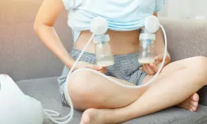Frau sitzt auf Sofa, beim abpumpen kommt kaum milch. Zwei Fläschchen mit wenig Milch sind an Doppel-Milchpumpe angeschlossen.