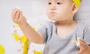 Kleines Kind mit gelbem Haarband isst mit den Händen, das Gesicht ist voller Polenta.