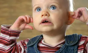 Kleines Baby kratzt sich am Ohr, die Augen weit aufgerissen.