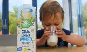 Ein süßes Kleinkind trinkt Soja Drink Calcium. Die Packung steht daneben.