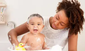 Mutter wäscht ihr Kind mit Fieber in der Wanne. Ein gelber Quietsche-Ente schwimmt mit.