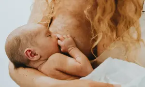 Ein Baby schreit beim Stillen, die Mutter hält es liebevoll.