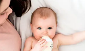 Ein Baby trinkt aus einer Flasche, während eine Person daneben liegt. Die Frage, wie lange braucht Essen bis es beim Baby ankommt, beschäftigt viele Eltern.