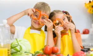 Zwei Kinder mit Paprikaringen vor den Augen, die Spaß beim Kochen haben. Ein wichtiger Aspekt für gesunde Entwicklung ist der richtige kalorienbedarf kind 10 jahre.