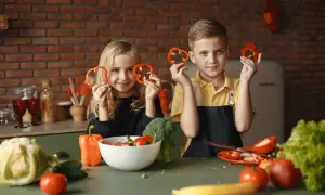 Zwei Kinder halten Paprikaringe hoch. Sie lernen, was muss man essen um zu wachsen: viel Gemüse!