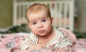 Baby mit blauen Augen liegt auf dem Bauch, sabbert und übt den 4 monats schub.