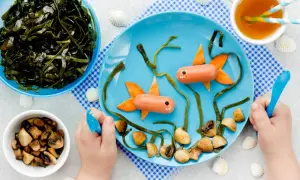 Kreativer Fischbrei für Babys: Würstchen-Fische schwimmen im Meer aus Algen und Pilzen auf einem blauen Teller.