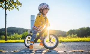 Kleiner Junge mit Helm auf Laufrad, strahlend im Sonnenuntergang. Ein echter Entwicklungsschub mit 3 Jahren!
