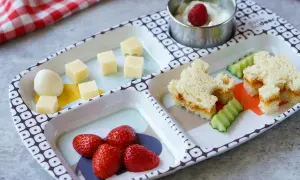 Leckeres Essen für ein Kleinkind (2 Jahre): Erdbeeren, Käsewürfel, ein Ei, Gurkenscheiben und ein süßes Sandwich.
