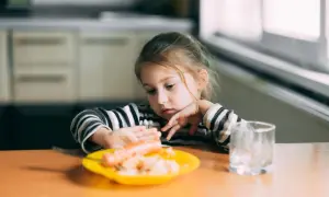 Ein kleines Mädchen mit nachdenklichem Blick betrachtet eine Wurst auf ihrem Teller. Typisches Essverhalten Kinder.
