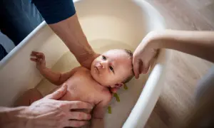 Eltern helfen ihrem Baby beim Duschen in einer Babybadewanne. Sanfte Hände halten das Kleine, während es im Wasser planscht.