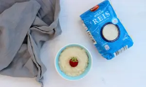 Ein Schälchen Milchreis mit Erdbeere, daneben eine Packung Milchreis. Perfekt für kleine Genießer.