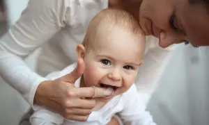 Ein Baby mit einem Daumen, der sanft die Zähne berührt, um die Zahnen Symptome zu lindern. Die Mutter küsst das Kind liebevoll.