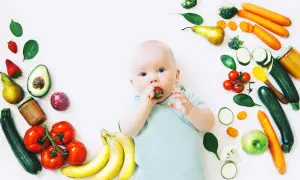 Baby mit Erdbeere im Mund, umgeben von Obst und Gemüse, das für die Lebensmittel und Milchbildung wichtig ist.