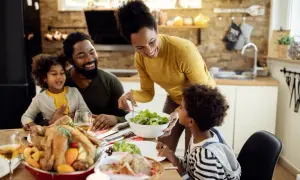 Familie am Esstisch, die ein Festessen genießt. Die Mutter reicht dem Sohn Salat, der wie mein Kind isst nicht 10 Jahre, hoffentlich probiert er.