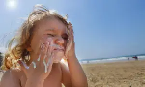 Kind schmiert sich Sonnencreme ins Gesicht. Bei Sonnenbrand helfen Hausmittel wie Quark oder Aloe Vera.