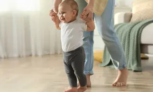 Ein Baby lernt laufen, gehalten von einer Person. Die ersten Schritte sind aufregend, wann stehen Babys?