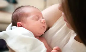Ein Neugeborenes schläft friedlich in den Armen seiner Mutter. Die Nähe und Wärme zeigen die vielen Vorteile stillen.