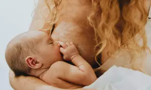 Ein Baby trinkt an der Brust, sein Kalorienbedarf wird auf natürliche Weise gestillt. Die Mutter hält es liebevoll.