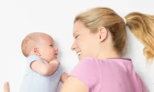 Ein lächelndes Baby, 2 Wochen alt, schaut seine Mutter an. Sie liegt neben ihm und lächelt zurück.