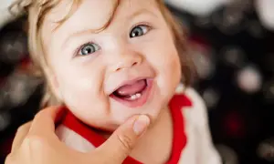 Ein Baby lächelt und zeigt stolz seinen ersten Zahn.