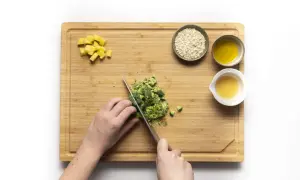 Hände schneiden Brokkoli für Babybrei. Kartoffelwürfel, Haferflocken und Öl sind bereit.