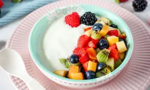 Ein Schüsselchen Joghurt mit frischem Obstsalat, perfekt für ein Kleinkind. Erdbeeren, Blaubeeren, Kiwi und Pfirsichstücke machen den Joghurt zum Genuss.