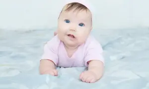Blauäugiges Baby in rosa Strampler und Mütze. Mögliche kiss-syndrom symptome wie Kopfhaltung können hier nicht erkannt werden.