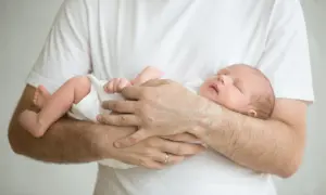 Ein Vater hält sein schlafendes Baby. Das Baby wedelt mit Armen und Beinen im Schlaf.