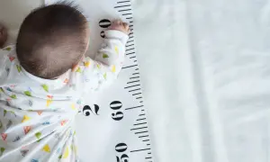 Baby liegt auf einer Messlatte, die als **Kleinwuchs Tabelle** dient. Die Messlatte zeigt Zentimeterangaben.