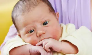 Ein süßes Baby mit schielenden Augen, das nachdenklich auf seinen Fingern kaut.