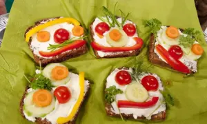 Lustige Gesichter auf belegten Broten: Fingerfood, das Kinder lieben. Bunte Gemüsesorten wie Paprika, Gurke und Karotte schmücken die Brotscheiben.