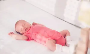Ein schlafendes Baby in einem pinken Strampler streckt sich durch, während es in seinem Bettchen ruht.