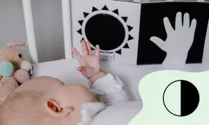 Ein Baby mit 2 Wochen erkundet mit seiner Hand ein Schwarz-Weiß-Buch mit Sonne und Hand.