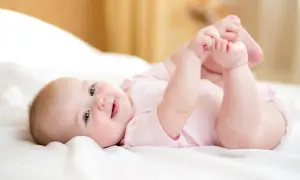 Ein lächelndes Baby von 8 Wochen liegt auf dem Rücken und spielt mit seinen Füßen.
