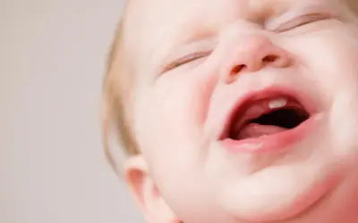 Ein Baby weint, weil es zahnt. Ein kleiner Zahn bricht durch das Zahnfleisch.