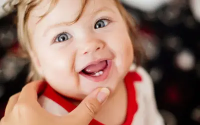 Ein Baby lächelt und zeigt stolz seinen ersten Zahn.