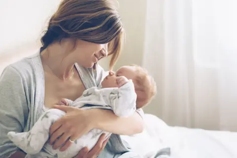 Mutter hält ihr Neugeborenes liebevoll im Arm. Ein Moment purer Zuneigung, eine stille Empfehlung für die innige Bindung zwischen Mutter und Kind.