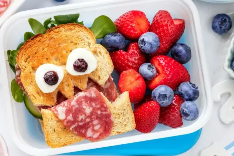 Ein lustiges Vesper-Essen Kita: ein Toast-Gesicht mit Wurst, Gurke und Beeren.