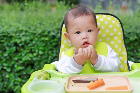 Ein süßes Baby isst im Hochstuhl. Der **Kalorienbedarf Baby 10 Monate** ist wichtig für seine Entwicklung.