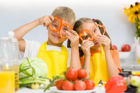 Zwei Kinder mit Paprikaringen vor den Augen, die Spaß beim Kochen haben. Gesunde Ernährung ist wichtig für den **Kalorienbedarf Kleinkind**.
